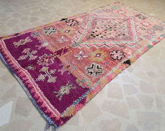 May include: A pink and purple Moroccan rug with intricate floral patterns. The rug has a distressed look and is made of wool.