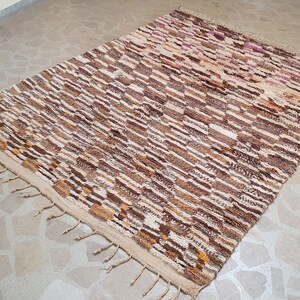 May include: A brown and white striped rug with a geometric pattern. The rug has a fringe border and is made of wool.