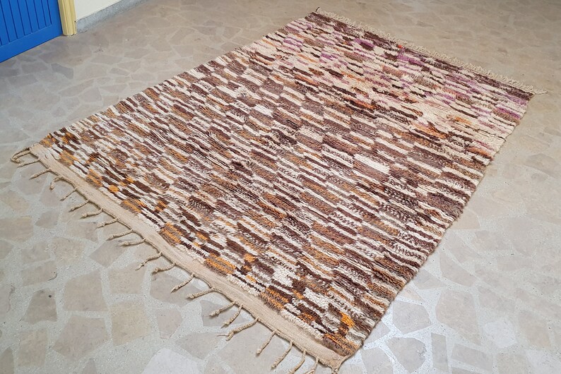 May include: A brown and white striped rug with a geometric pattern. The rug has a fringe border and is made of wool.