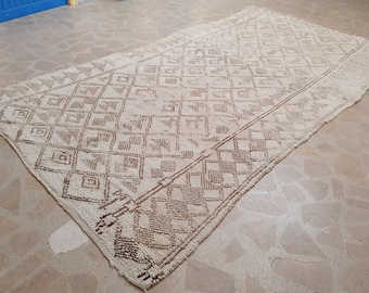 May include: A white and brown patterned rug with a geometric design. The rug has a fringed edge and is made of a soft, woven material.