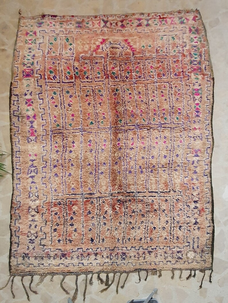 May include: A vintage Moroccan rug with a beige background and intricate patterns in shades of purple, pink, green, and brown. The rug has a fringe border and a geometric design.