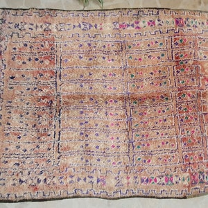 May include: A vintage Moroccan rug with a geometric pattern in shades of brown, purple, green, and pink. The rug has a fringe border and is woven with a variety of textures.