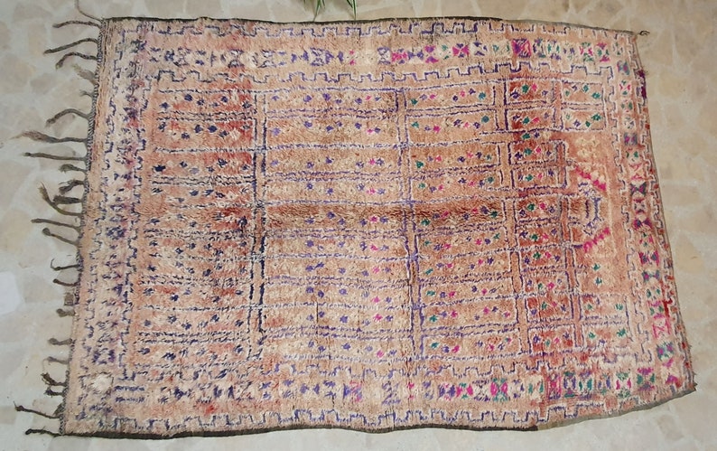 May include: A vintage Moroccan rug with a geometric pattern in shades of brown, purple, green, and pink. The rug has a fringe border and is woven with a variety of textures.