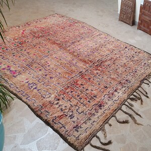 May include: A vintage Moroccan rug with a brown, red, and purple geometric pattern. The rug has fringe on all sides and is made of wool.