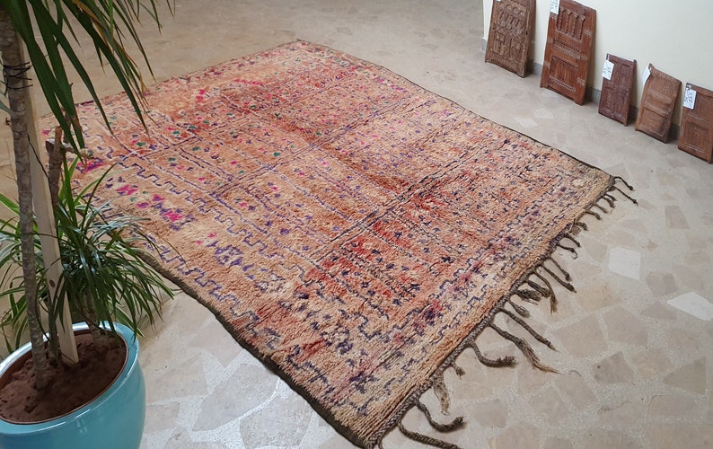 May include: A vintage Moroccan rug with a brown, red, and purple geometric pattern. The rug has fringe on all sides and is made of wool.