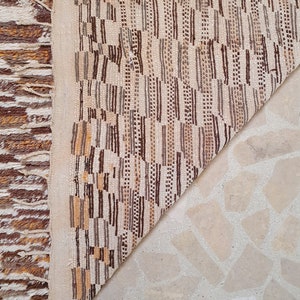 May include: Close-up of the back of a brown and white woven rug with a geometric pattern. The rug is folded in half, revealing the white backing.