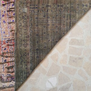 May include: Close-up of the back side of a rug with a geometric pattern in shades of brown and green. The rug has fringe along the edges.
