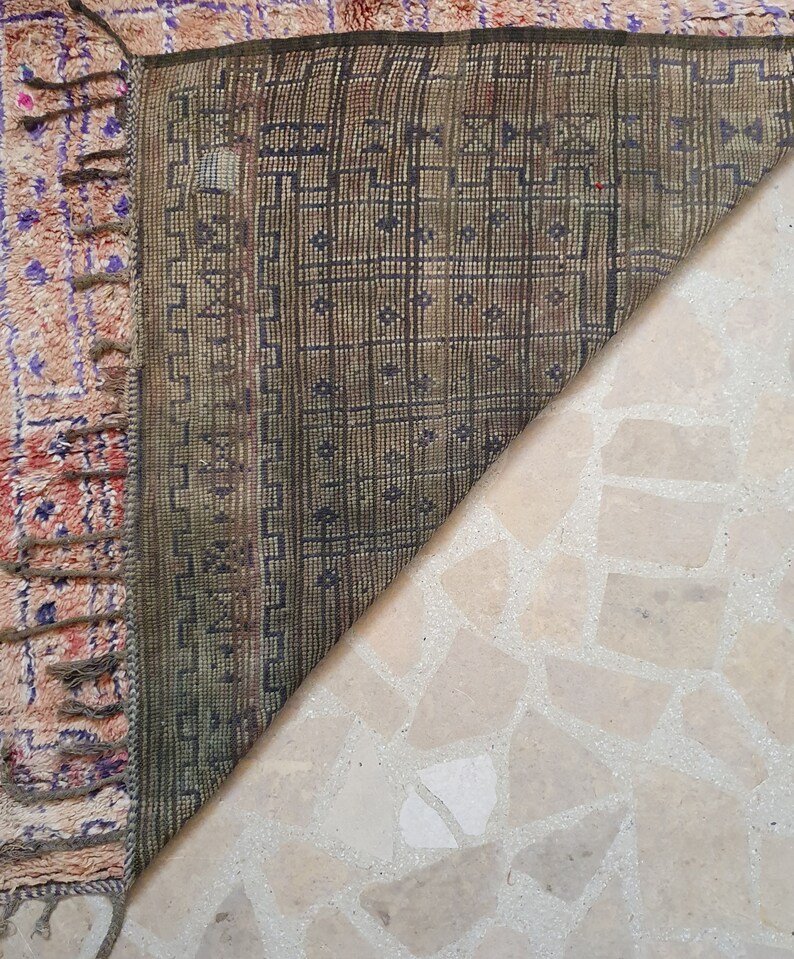 May include: Close-up of the back side of a rug with a geometric pattern in shades of brown and green. The rug has fringe along the edges.