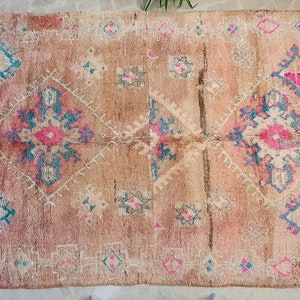 May include: A vintage Moroccan rug with a beige background and intricate geometric patterns in shades of pink, blue, and white.