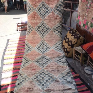 Puede incluir: Una alfombra larga y rectangular con un patrón de diamantes en tonos de rosa, azul y blanco. La alfombra está hecha de un material suave y esponjoso y tiene un aspecto desgastado y vintage.