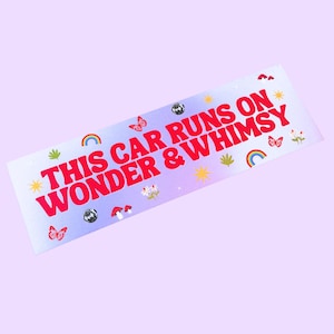 May include: A rectangular bumper sticker with a light purple background. The sticker has the text "THIS CAR RUNS ON WONDER & WHIMSY" in red. It is decorated with butterflies, rainbows, and stars.