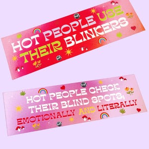 May include: Two rectangular stickers with text. The top sticker is red with the words "HOT PEOPLE USE THEIR BLINKERS" in white and green. The bottom sticker is pink with the words "HOT PEOPLE CHECK THEIR BLIND SPOTS; EMOTIONALLY AND LITERALLY".