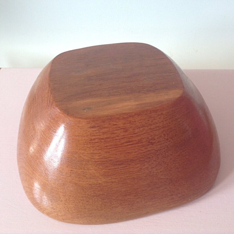 May include: A large, wooden bowl with a rounded, square shape. The bowl is made of light brown wood and has a smooth, polished finish.