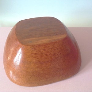 May include: A large, wooden bowl with a smooth, rounded shape. The bowl is made of light brown wood and has a natural, polished finish.
