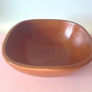 May include: A large, square wooden bowl with a smooth, natural finish. The bowl is empty and appears to be made of light brown wood.