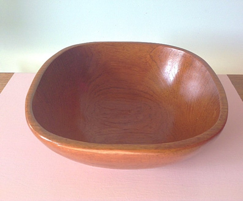 May include: A large, square wooden bowl with a smooth, natural finish. The bowl is empty and appears to be made of light brown wood.