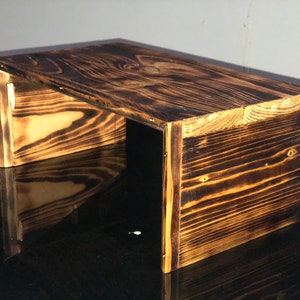 Puede incluir: Un estante de madera rústico con un acabado marrón oscuro quemado. El estante está hecho de madera recuperada y tiene un aspecto único y artesanal.