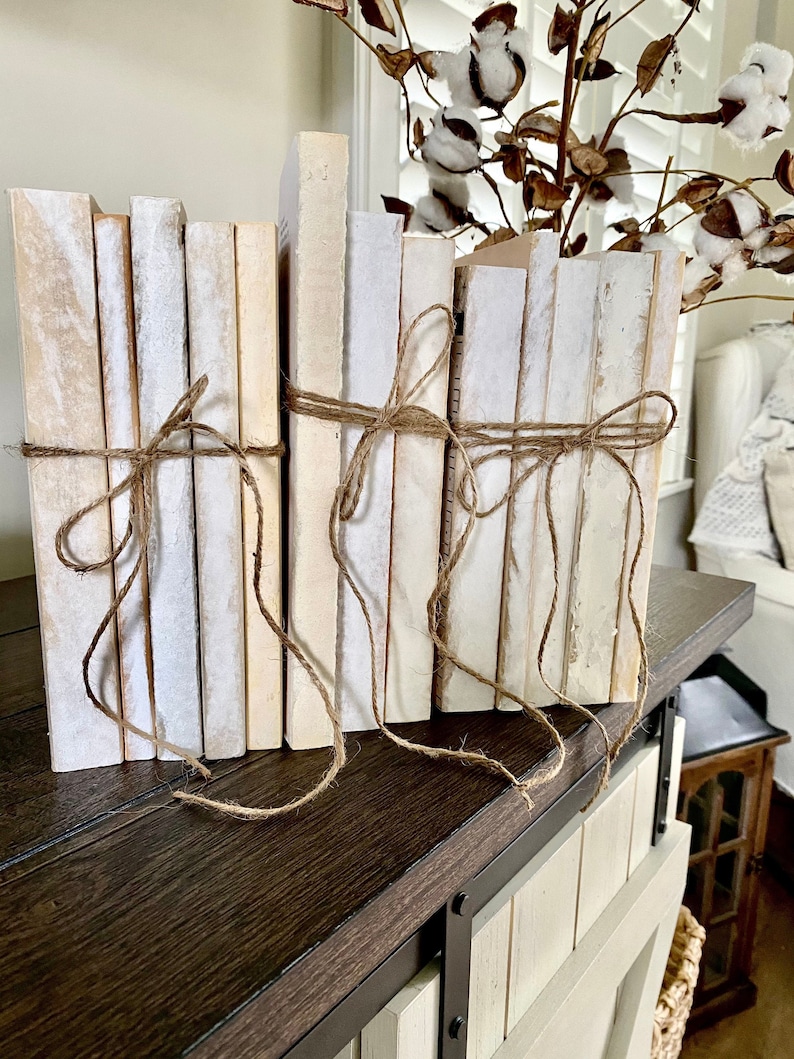May include: A stack of white and cream coloured books tied together with twine. The books are arranged on a dark brown wooden surface.