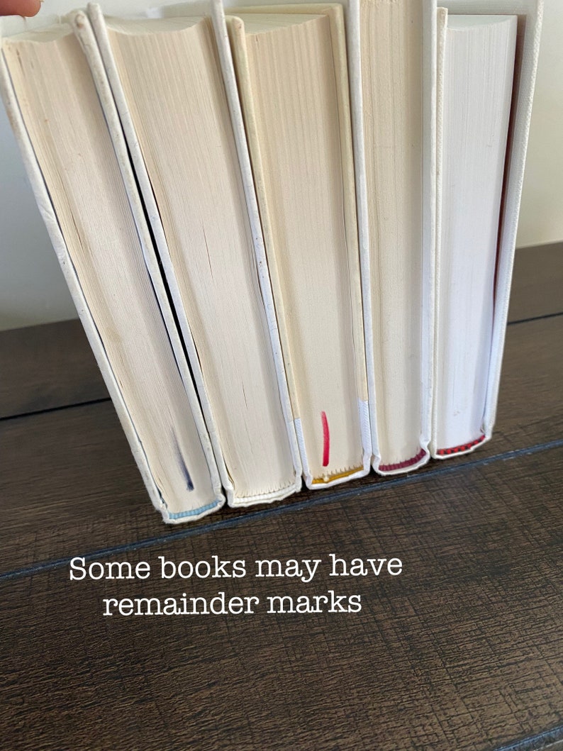 May include: A row of hardcover books with off-white covers and spines. The text "Some books may have remainder marks" is visible. The edges of the pages are visible, and some books have colored marks.