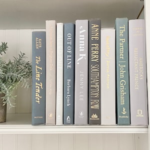 May include: A bookshelf with a variety of books in different shades of gray and white. The books have gold lettering on the spines and include titles like "The Line Tender", "Called Out", "Out of Line", "Anna K", "Anne Perry Southampton Row", "Loveatrey", "The Partner", "America's Reluctant Prince".