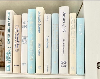 May include: A bookshelf with a collection of books in various shades of blue and white. The books have titles such as "The Mermaid Chair", "The Lido", "Invincible Summer", "Summer of '69", and "Cool It".