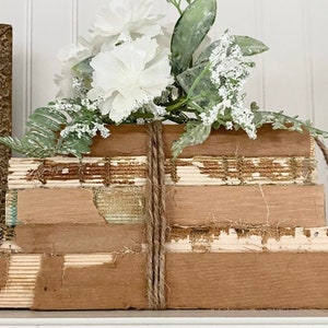 May include: A stack of vintage books wrapped in twine with a bouquet of white flowers on top. The books are brown and have a rustic look.