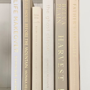 May include: A bookshelf with a collection of books with gold lettering on the spines. The books are arranged in a row from left to right. The titles of the books are "Life Makeover", "Last House Before the Mountain", "Bring Your Baggage and Don't Pack Light", "The Ghost Clause", "Belva Plain Harvest", and "My Father's Day Gift".