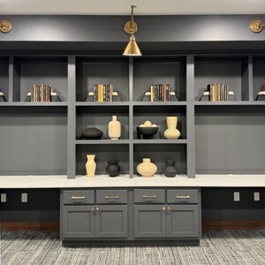 May include: A dark gray built-in bookshelf with white countertops and gray cabinets. The shelves are filled with books and decorative vases. The room has a modern design.