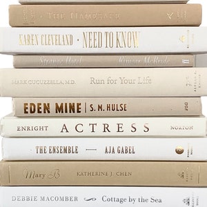May include: A stack of ten beige and white paperback books with gold lettering. The titles include "OK, Mr. Field", "The Namesake", "Karen Cleveland - Need to Know", "Strange Hotel", "Run for Your Life", "Eden Mine", "Actress", "The Ensemble", "Mary B", and "Cottage by the Sea".