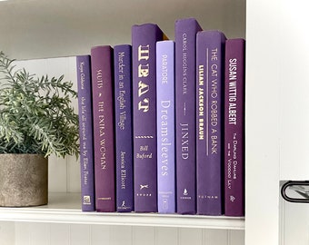 May include: A bookshelf with a variety of purple and blue hardcover books. The titles of the books include "Heat", "Dreamsleeves", "Jinxed", "The Cat Who Robbed a Bank", "The Darling Dahlias and the Voodoo Lily", "Scutts: The Extra Woman", "Murder in an English Village", and "The Life All Around Me by Ellen Foster".