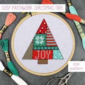 May include: A cross-stitch pattern for a Christmas tree with a patchwork design. The tree is red, green, and white with the word "JOY" in the center. The pattern is in a wooden embroidery hoop.