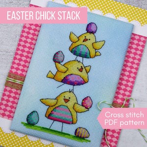 May include: Cross-stitch PDF pattern showing a stack of three yellow chicks holding colourful eggs. The design is on a light blue background with the text "Easter Chick Stack" and "Cross stitch PDF pattern". The background has pink and white patterns.