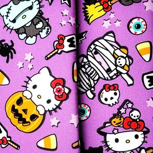 May include: A purple Halloween-themed accessory set featuring a repeating pattern of cartoon characters, candy corn, and stars. The set includes a wrist strap and two larger items, possibly a wallet or organizer. The design features a witch, mummy, and other spooky characters.