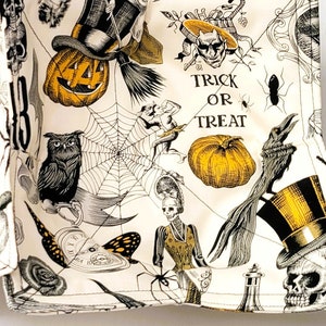 May include: Two white fabric Halloween-themed square coasters with a black and yellow print. The print features a variety of Halloween imagery, including pumpkins, owls, bats, skulls, and a witch's broom. The text "Trick or Treat" is printed on each coaster.