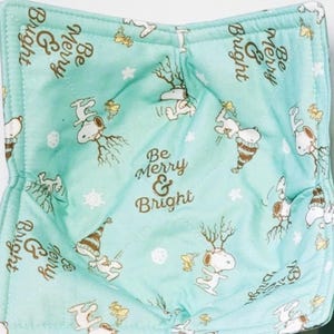 May include: Two aqua-colored bowl cozies and two matching coasters. The fabric features a repeating pattern of a cartoon character in a winter hat, snowflakes, and the text "Be Merry & Bright".