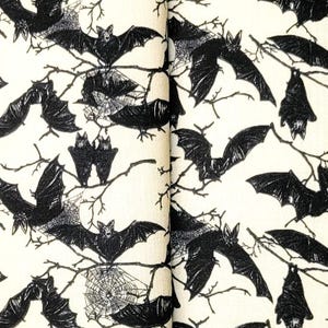 May include: A cream-colored wallet and matching wristlet featuring a black bat and branch pattern. The wallet is folded, and the wristlet has a metal ring. The design is repeated on both items.