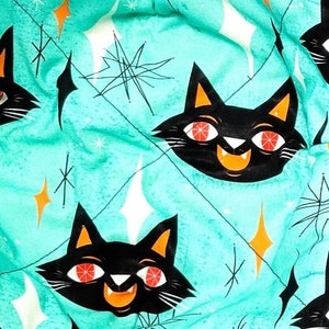 May include: Two teal blue quilted pot holders with a black cat pattern and orange eyes. The cats are smiling and have a retro mid-century modern design. The background is a teal blue with white stars.