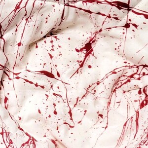 May include: Two white fabric bowls with a red splatter paint design. The bowls are folded and have a quilted texture.