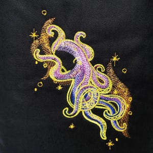 May include: Embroidered design of a purple and yellow octopus with a swirling background of gold and brown. The octopus is surrounded by small gold stars.