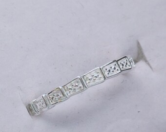 May include: A silver ring with a row of small, square-shaped stones set in a band.