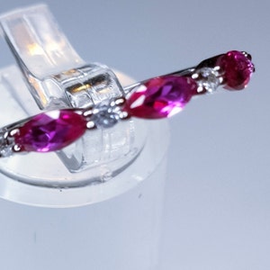 Op de afbeelding: Een zilveren ring met drie roze ovale edelstenen en een kleinere, heldere edelsteen in het midden.