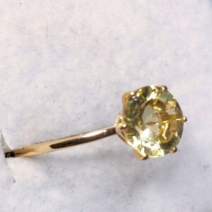 May include: A gold ring with a large, round, yellow gemstone set in a prong setting.