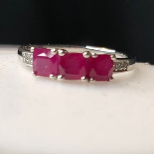 May include: A silver ring with three red ruby stones and small diamonds set in the band.