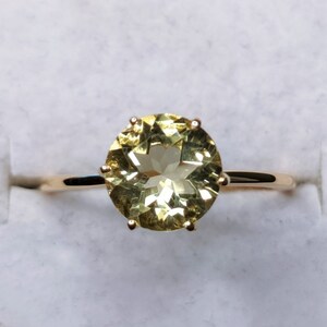 May include: A gold ring with a large, round, light green gemstone set in a prong setting.