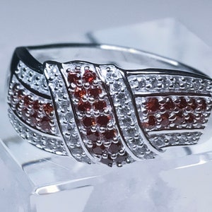 May include: A silver ring with a twisted design featuring red and white gemstones.