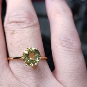 May include: A gold ring with a round, light green gemstone set in a prong setting.