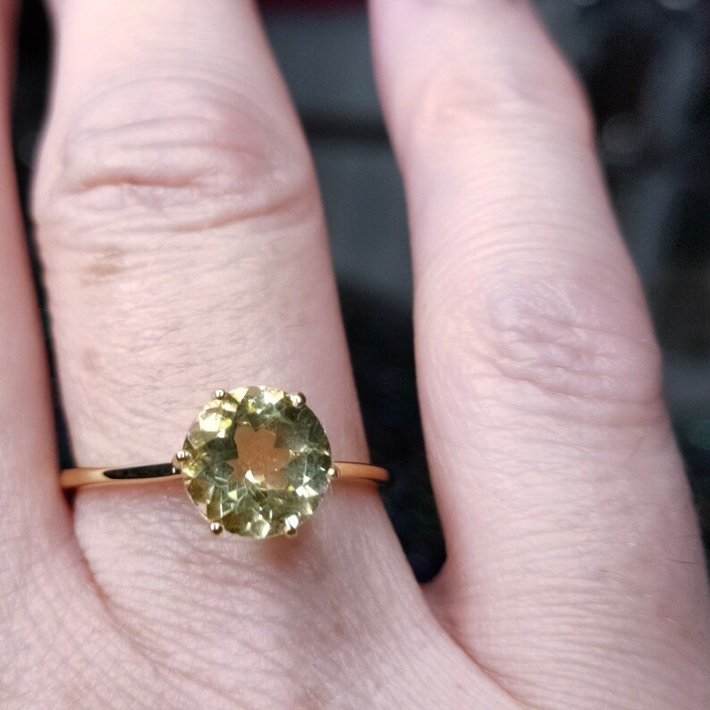 May include: A gold ring with a round, light green gemstone set in a prong setting.