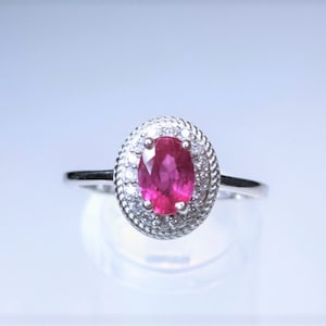 May include: A silver ring with a large oval-shaped ruby gemstone surrounded by a halo of smaller diamonds.