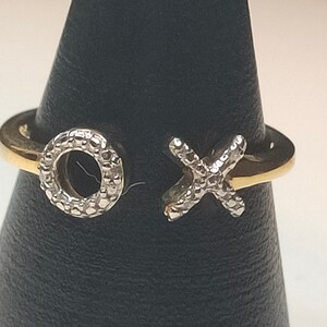 May include: A gold ring with two silver charms, one shaped like an 'O' and the other like an 'X'. Both charms are covered in small, sparkling stones.