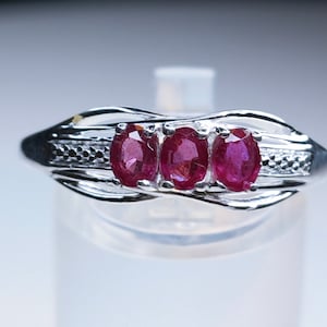 May include: A silver ring featuring three oval-shaped ruby gemstones set in a twisted band.